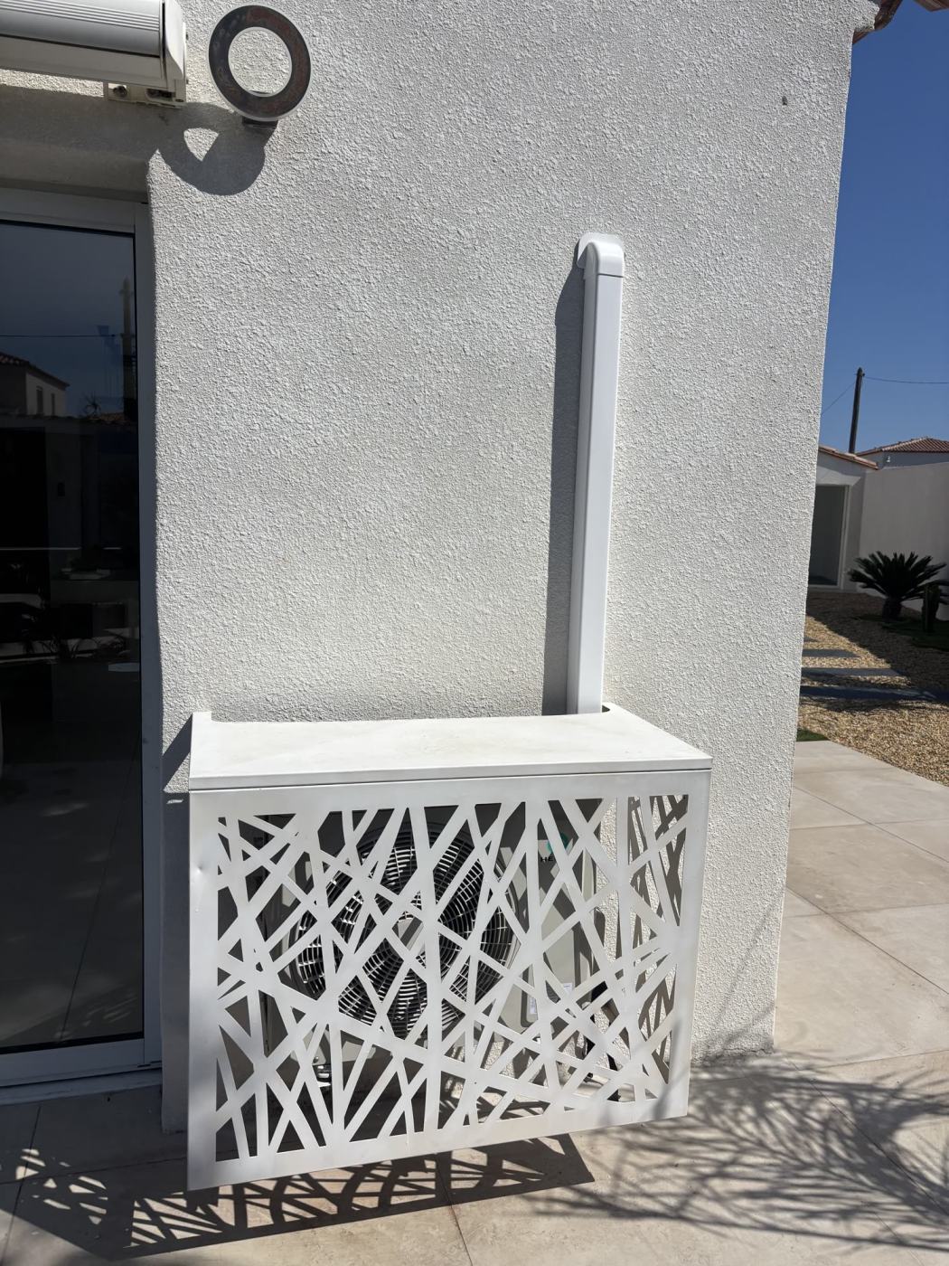 Groupe extérieur de climatisation habillé d'un cache décoratif ajouré, contre une façade blanche