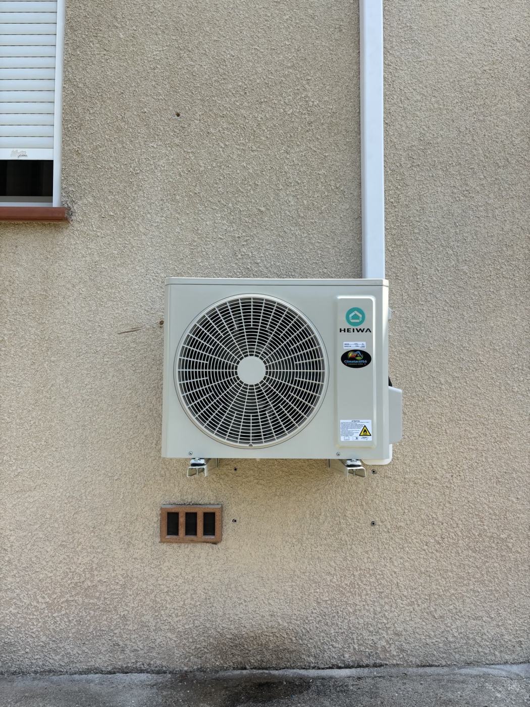 Groupe extérieur Heiwa posé sur équerres contre une façade crépie
